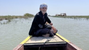 Marsh Arab sitting in a traditional wooden mashoof boat surrounded by the reed-lined waterways of the Mesopotamian Marshes in southern Iraq.