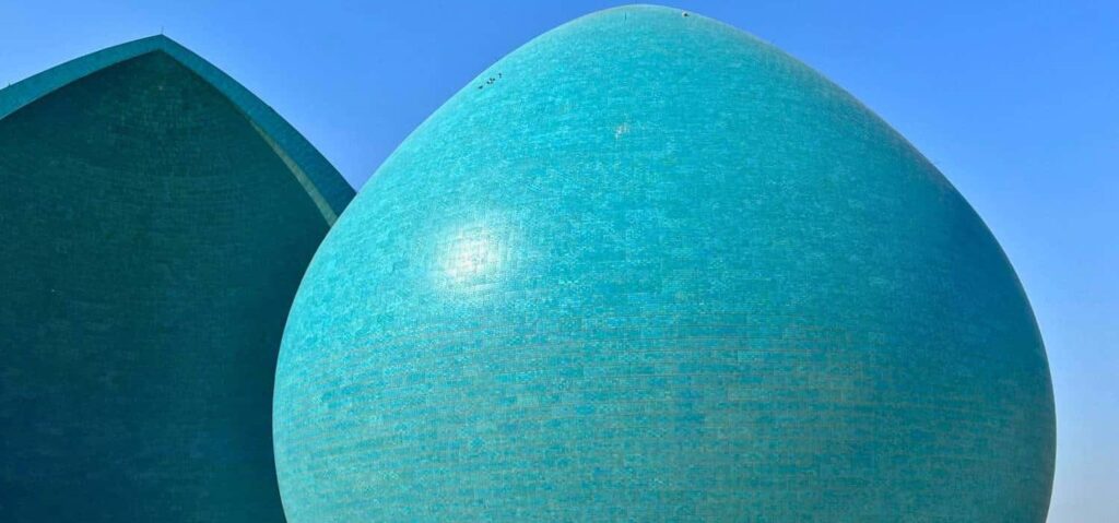 Striking architectural view of Baghdad's Martyr Monument in Iraq, showing the distinctive turquoise split dome rising above the surrounding landscape and reflecting one of the capital's most recognizable modern landmarks.