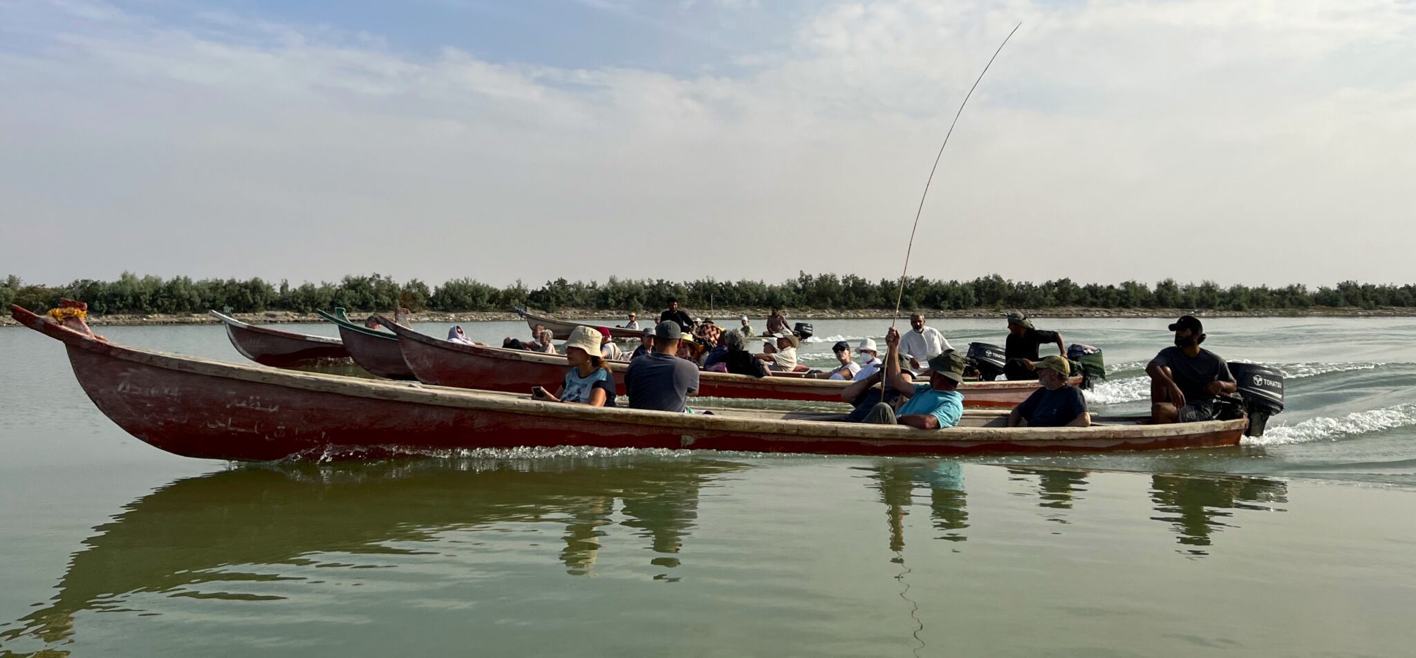 People traveling by traditional boat through the reed-filled waterways of the Mesopotamian Marshes in southern Iraq.