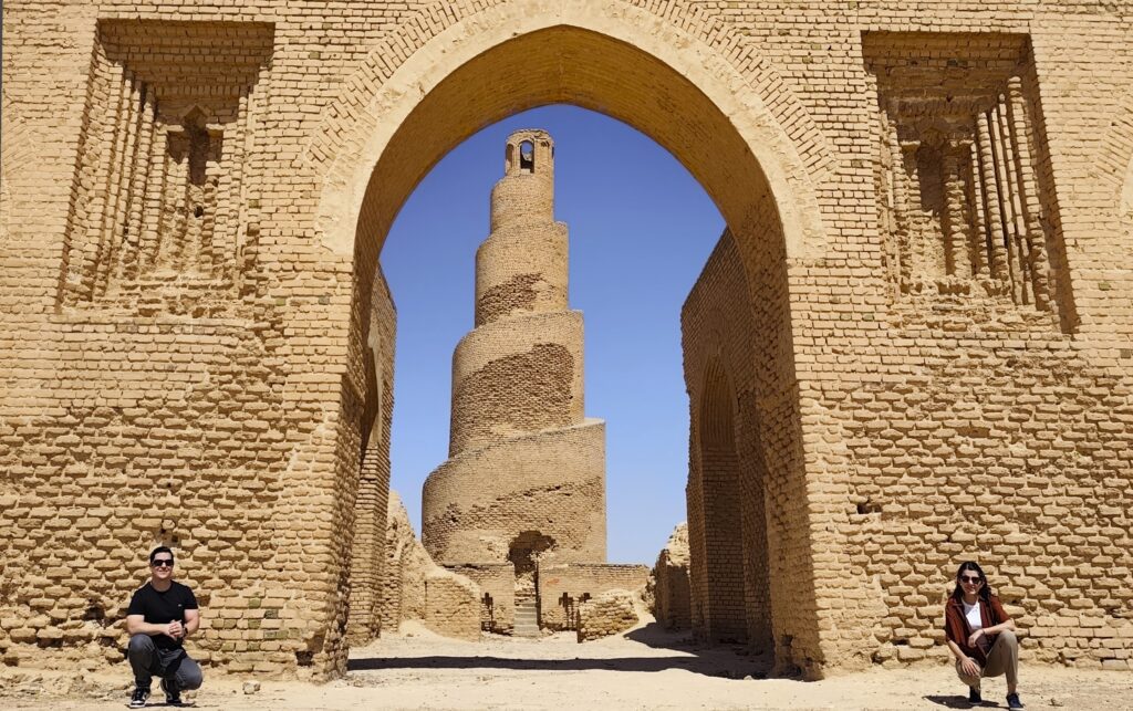 Tourist taking a photograph in front of Abu Dulaf Mosque and its distinctive spiral minaret in Samarra, Iraq, capturing the remarkable Abbasid architecture and expansive archaeological surroundings.