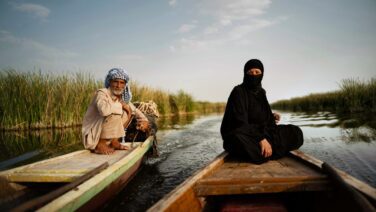 Marsh Arab man steering a traditional mashoof boat through the waterways of the Mesopotamian Marshes in southern Iraq, surrounded by reeds and the distinctive wetland landscape