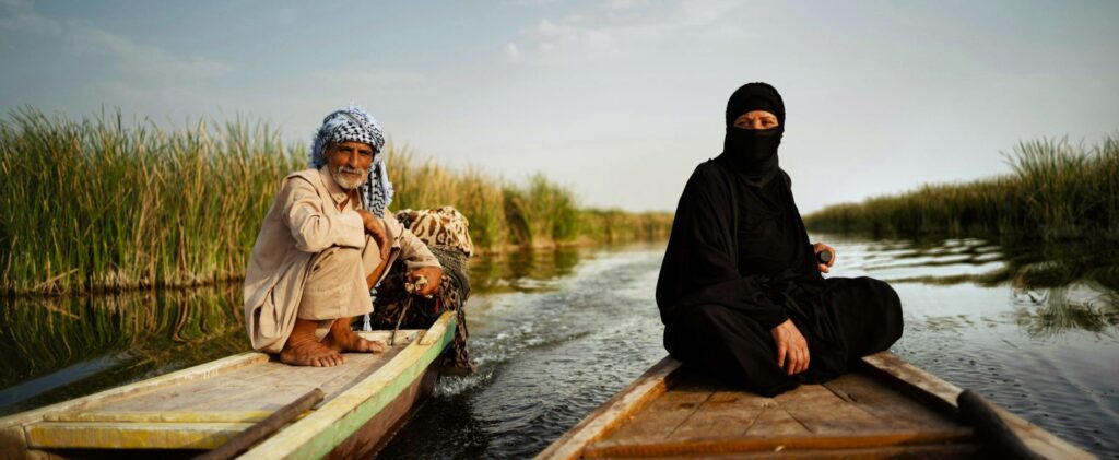 Marsh Arab man steering a traditional mashoof boat through the waterways of the Mesopotamian Marshes in southern Iraq, surrounded by reeds and the distinctive wetland landscape